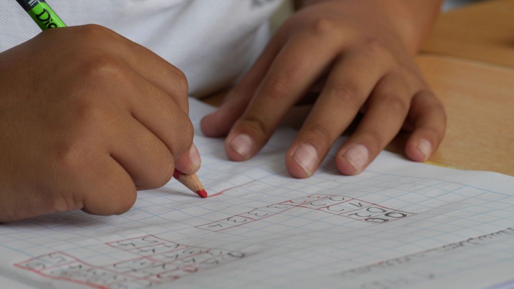 A close up of a Black child's hands writing in a school workbook with a pencil