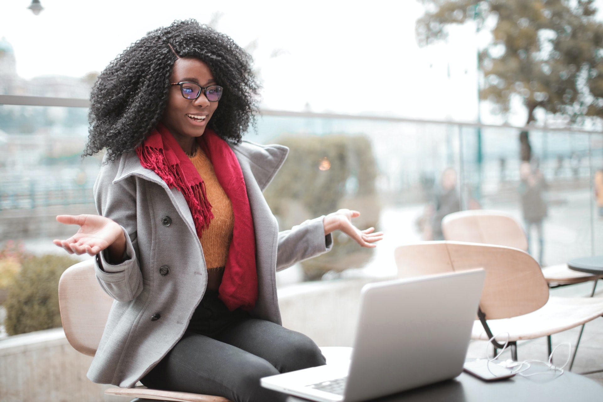 A Black woman with her natural afro textured hair worn freely is wearing office attire and talks infront of a laptop