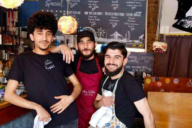 The photo shows three men smiling in a cafe, they are all refugees who have made a success of their new business in the UK