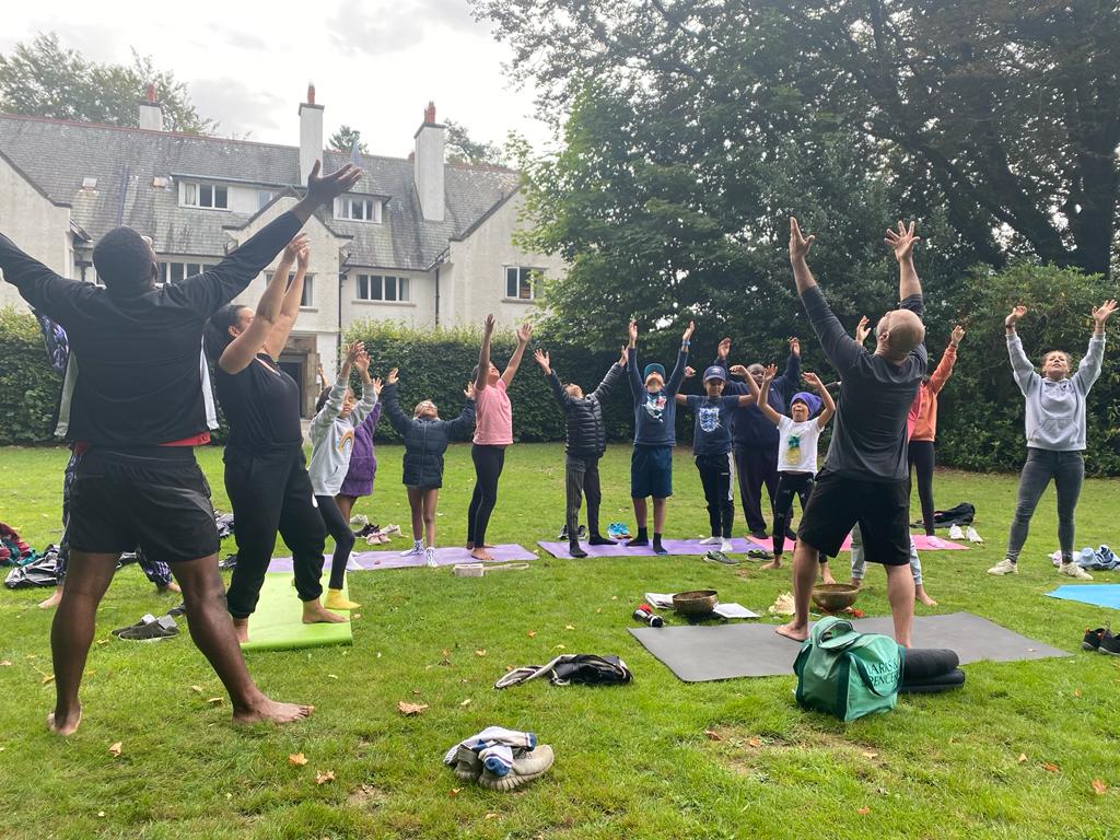 A group of Black and Brown Young People taking part in a yoga class outside on the grass