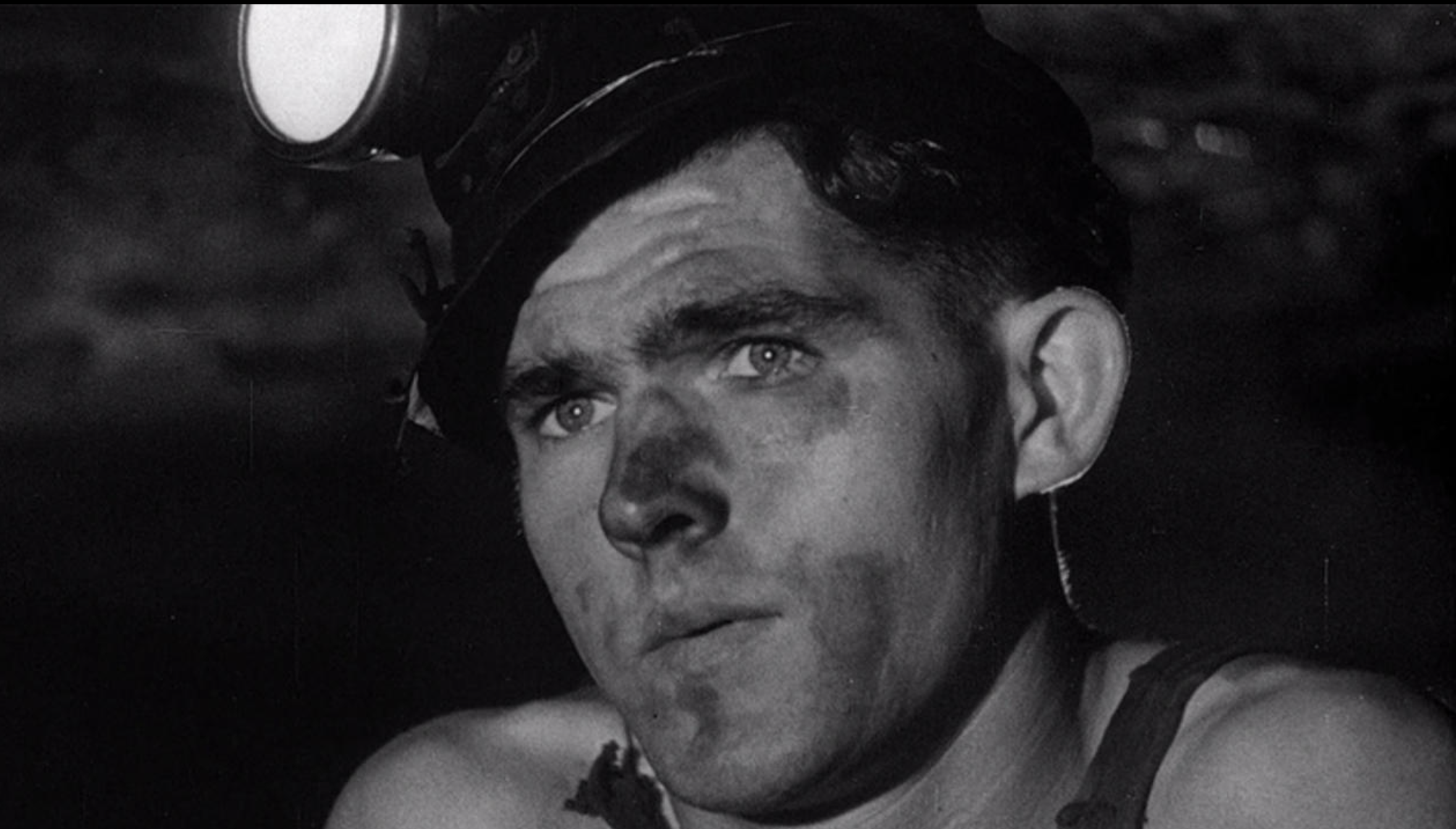 Still from a film. A young white man with coal on his face stares into the distance.