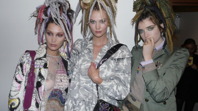 Three white models wear their hair in locks and long jackets in shades of grey, white and darker colours.