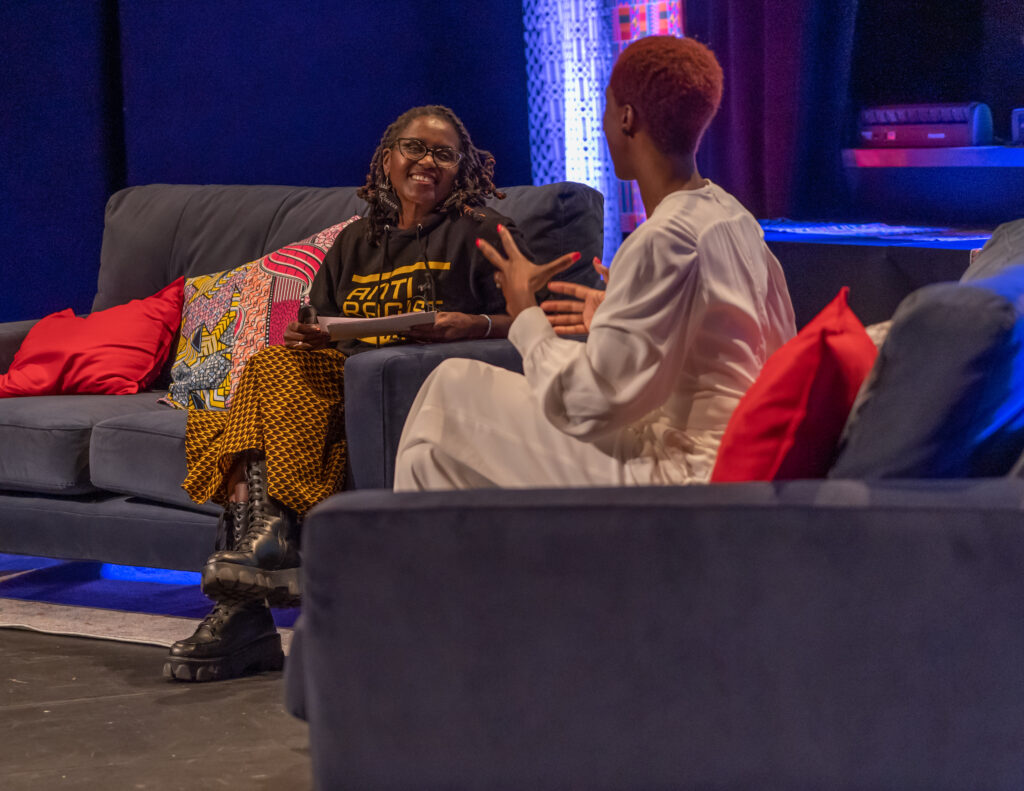 Two Black women converse on stage.