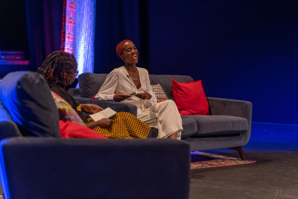 Two Black women converse as they sit on stage.