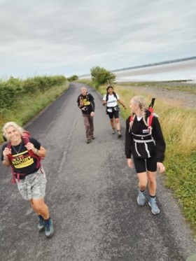 Four people walk along a road. They are turning to talk to each other.