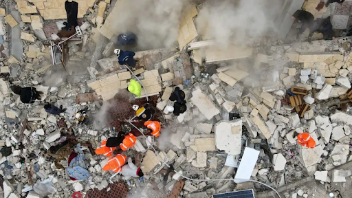 Overhead photo of people looking through smoking piles of rubble.