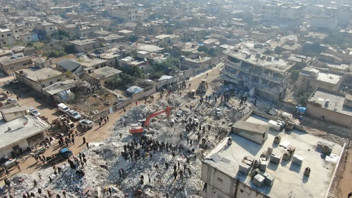 Overhead photo shows a red crane and many people on a huge pile of rubble where a building once stood
