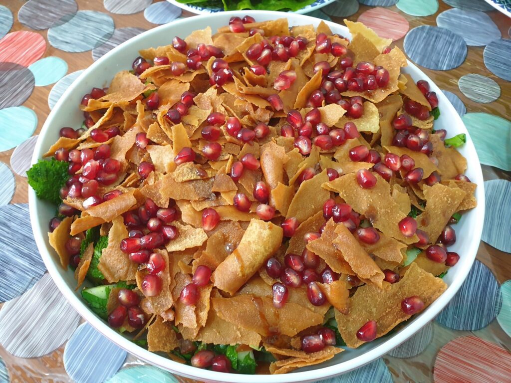 Golden brown thin crispy bread pieces cover a salad. Shiny red pomegrante seeds and honey are scattered and drizzled on top. 