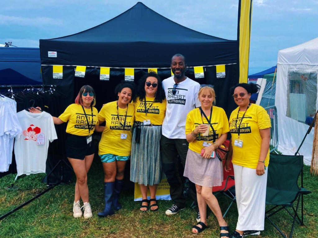6 Anti Racist Cumbria Volunteers in front of the ARC tent at Solfest 2023, all wearing Anti Racist Cumbria tees