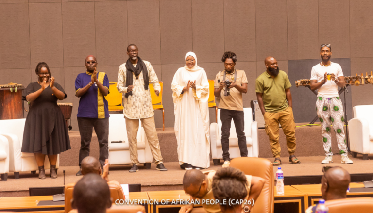 Image shows a line of Black people in bright, joyful outfits performing onstage.