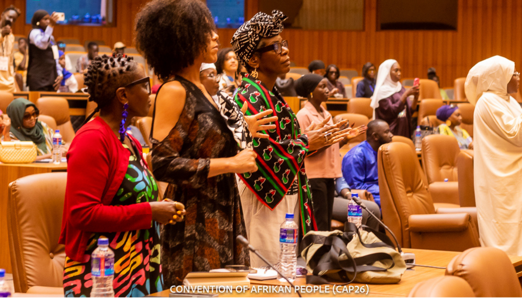 Image shows audience of Black people standing up and listening intently to a speaker.
